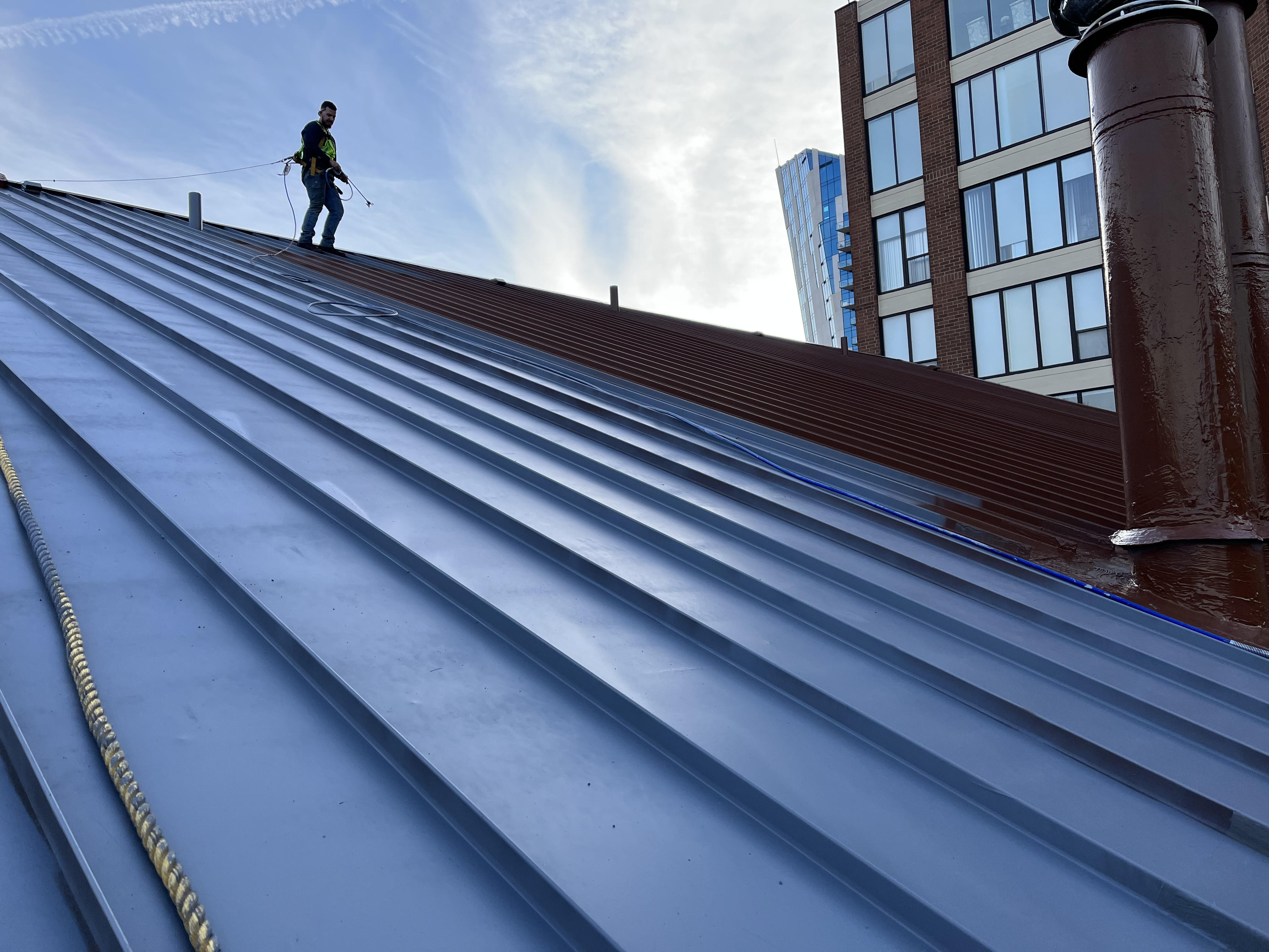 Gold Standard Coatings crew member on a new-construction standing-seam metal roof